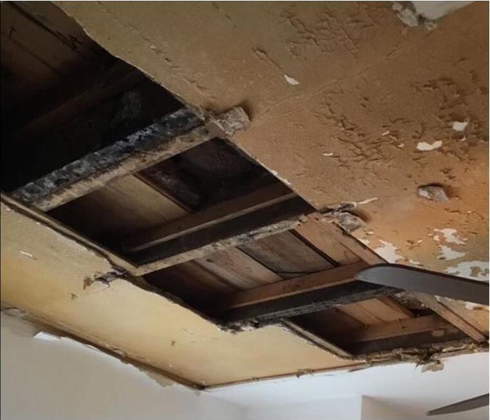 A ceiling with exposed beams, peeling and water damage.