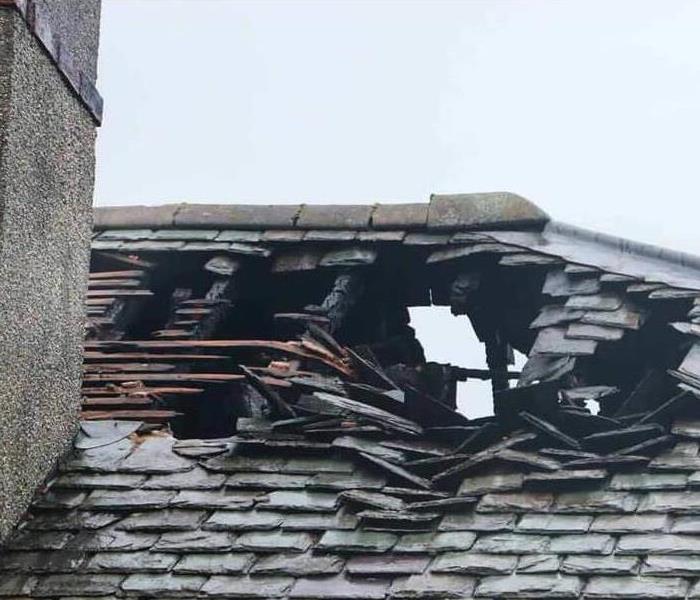 A roof that has been badly damaged by a fire, with hole in it. Next to the chimeny.